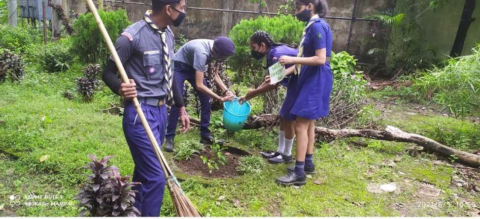 Students in scout and guide uniform planting and watering a sapling in the school garden